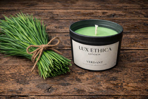 Verdant Green scented candle beside fresh chives on a wooden table.